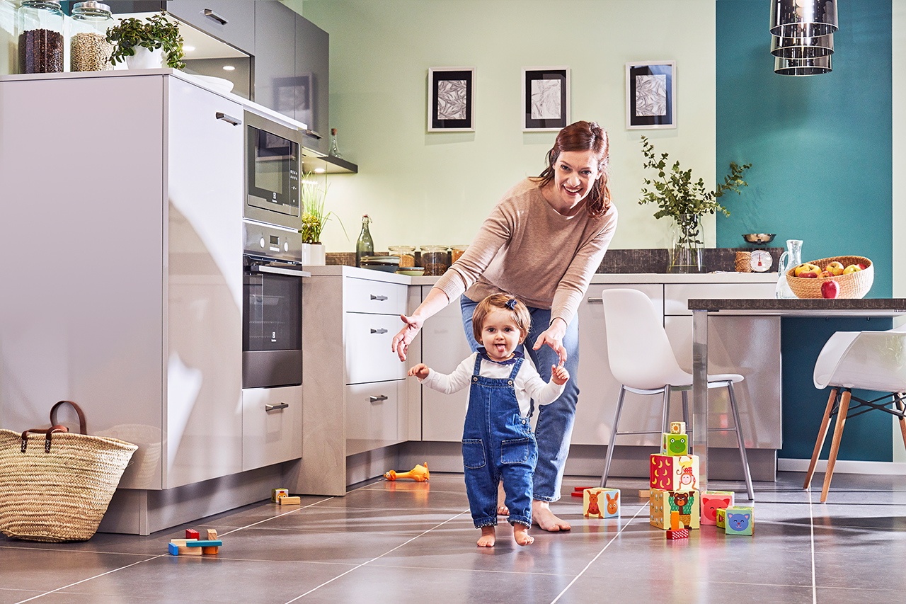 Photo lifestyle d'une maman et son bébé qui commence à marcher dans la cuisine